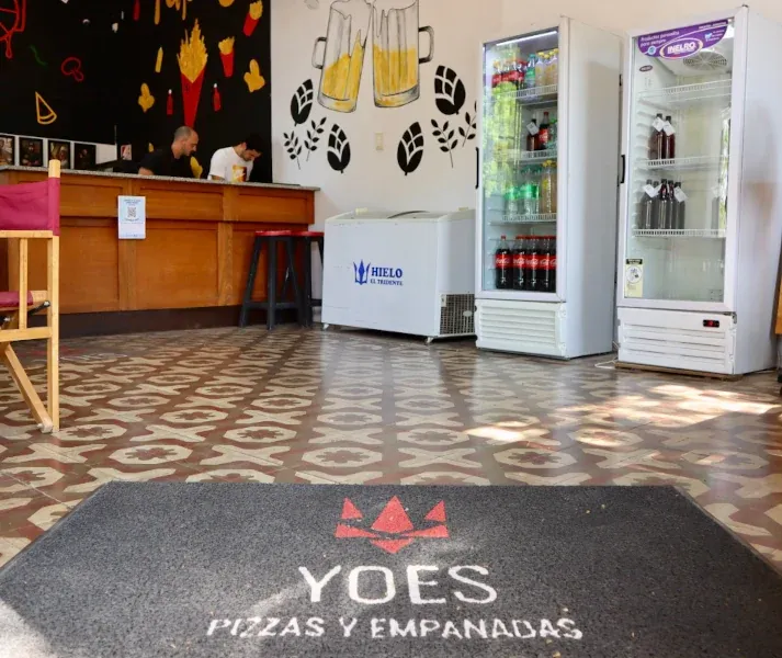 Adentro de YOES: mostrador, heladeras de bebidas y la alfombra con el logo