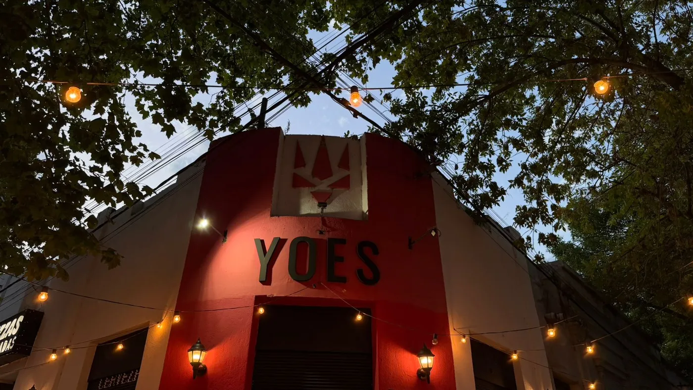 Fachada roja de YOES de noche, con luces colgantes, en San Martín y Alem, Trenque Lauquen